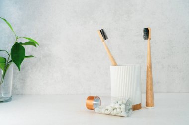 Sıfır atık banyo. Bambu diş fırçaları geri dönüşüm malzemesi kabında, doğal ağız yıkama tabletleri ve cam içinde taze yeşil bitkiler. Ağız bakımı gereklidir. Çevre dostu ev. Minimalizm. Boşluğu kopyala.