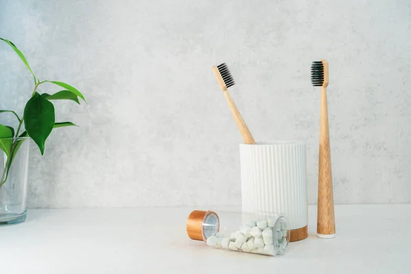 Μηδέν άχρηστα είδη μπάνιου. Οδοντόβουρτσες μπαμπού σε υποδοχέα υλικών ανακύκλωσης, φυσικές ταμπλέτες πλύσης στόματος και φρέσκα πράσινα φυτά σε γυαλί. Απαραίτητα για την στοματική φροντίδα. Οικολογικό σπίτι. Μινιμαλισμός. Αντιγραφή χώρου. — Φωτογραφία Αρχείου