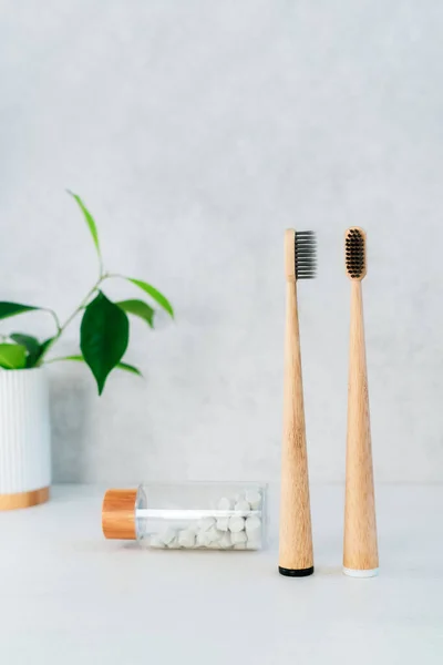 Zero waste bathroom items. Bamboo toothbrushes in recycling material holder, natural mouthwashing tabs and fresh green plants in glass. Oral care essentials. Eco-friendly home. Minimalism. Copy space. — Stock Photo, Image