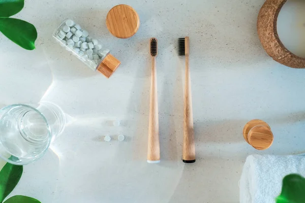 Top view zero waste bathroom items. Bamboo toothbrushes, natural mouthwashing tabs, fresh green leaves and glass of water on light background. Oral care essentials. Eco-friendly home. Minimalism. — Stock Photo, Image