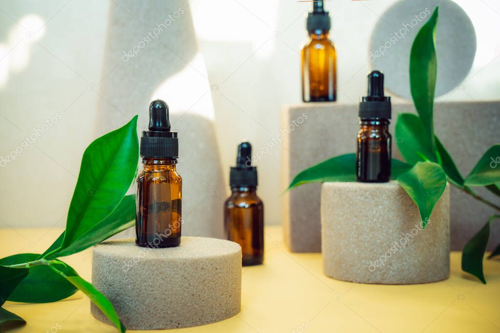 Creative background of geometric shapes with natural cosmetic essential oils bottles. Beauty and body care product concept on trendy stands or podiums with fresh green leaves. Sun light and shadows.