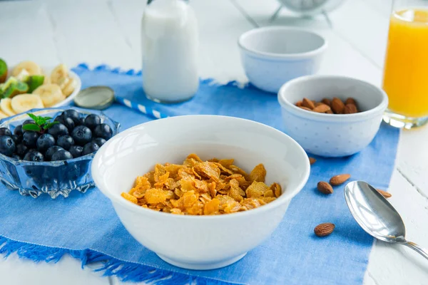 Nährstoffreiches gesundes Frühstück. Schüssel mit Müsli, Mandeln, Blaubeeren, pflanzlicher Milch und Orangensaft auf blauer Serviette und weißem Holztisch. Ernährungsplanung und gesundes Ernährungskonzept. — Stockfoto
