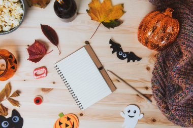 Üst görünüm boş defter ahşap masa üzerinde geleneksel Cadılar Bayramı dekoru, yarasalar, hayalet siluetleri, aydınlatma balkabağı, sonbahar yaprakları ve sıcak ekoseli. Sonbahar tatilinin samimi konsepti, Flatlay. Boşluğu kopyala