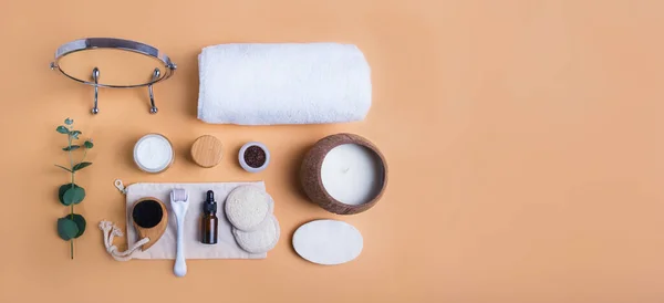 Top view home self-care kit for face. Dry lymphatic drainage massage brush, mezoroller, loofah pads, natural serum, scrab, cream, towel on beige background. DIY natural eco cosmetics and home spa.