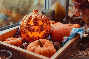 Pencerenin kenarındaki Cadılar Bayramı kompozisyonunu kapat. Işıklandırma kriko-fener, dekoratif balkabakları, koniler, ahşap tepside mumlar, sıcak ekose. Hygge cadılar bayramı ev dekoru. Seçici odak