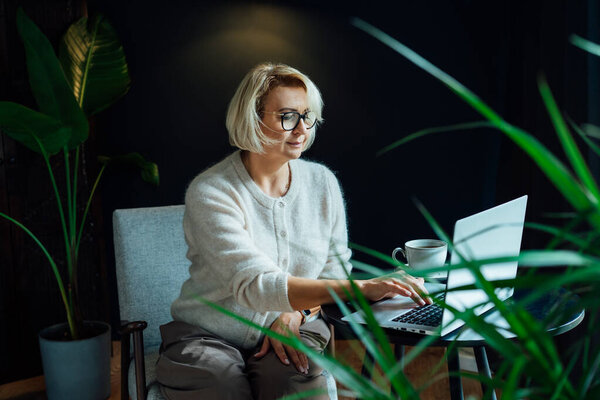 Smiling 50s stylish, confident mature businesswoman, middle aged experienced senior female professional, business coach, mentor, therapist, counselor working on laptop in office. Female leader
