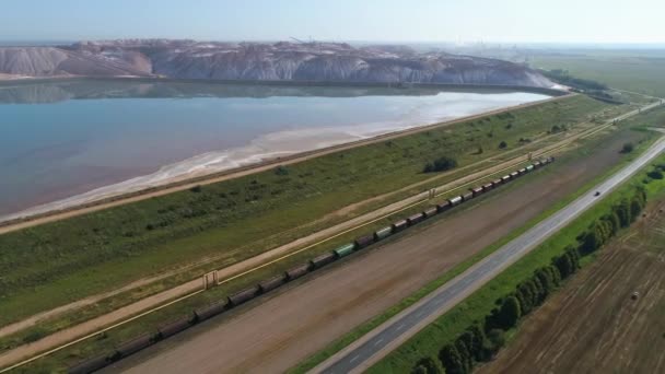 Tren viajando en ferrocarril cerca de montones de sal, vista aérea de canteras industriales de carga, vista desde la altura. — Vídeo de stock