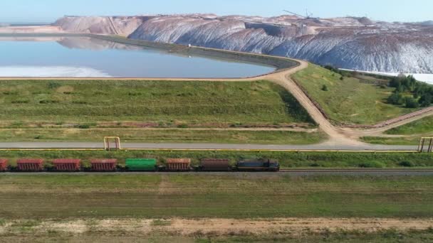 Treno che viaggia sulla ferrovia vicino a mucchi di sale, veduta aerea delle Cave industriali di trasporti, vista dall'altezza. — Video Stock