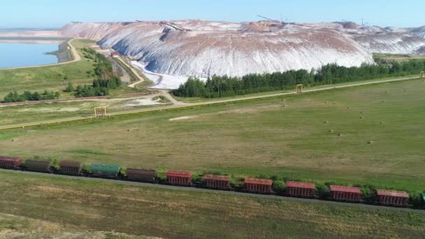 Frete trem viajando na estrada de ferro perto de montes de sal, vista aérea da pedreira industrial, vista de altura. — Vídeo de Stock