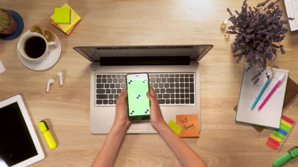 Garota na mão mantém smartphone com tela verde, swiping e toque na tela, sentado à mesa de trabalho, visão em primeira pessoa. — Vídeo de Stock