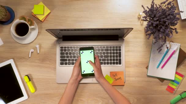 La ragazza mantiene in mano smartphone con schermo verde, strisciando e tocco sullo schermo, seduto al tavolo di lavoro, vista in prima persona. — Video Stock