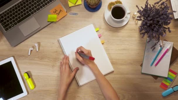 Dívka píše na kousek papíru a fráze - nyní, u pracovního stolu, first-person pohled rukou. — Stock video