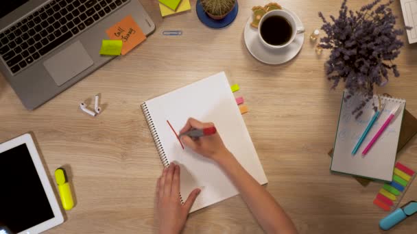 Menina escreve em um pedaço de papel uma frase - Freelance, sentado à mesa de trabalho, visão em primeira pessoa de mãos. — Vídeo de Stock