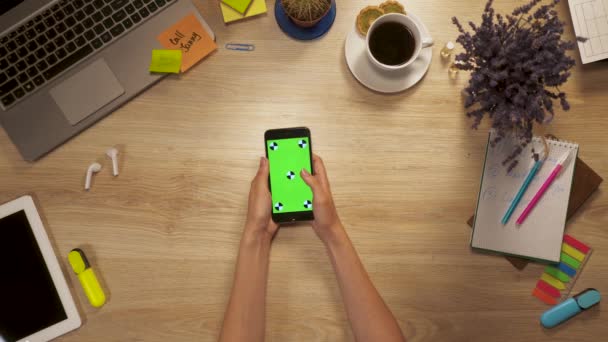 Girl keeps in hand smartphone with green screen, swiping and tap on screen, sitting at work table, first-person view. — Stock Video