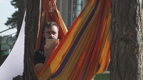 Uomo si trova su un'amaca in natura, utilizza una tavoletta di schermo. — Video Stock