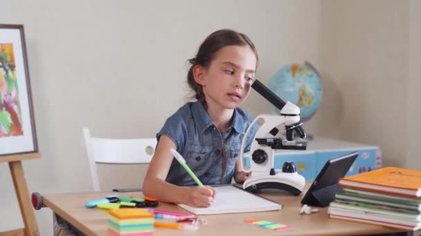 Schoolmeisje huiswerk, op zoek door middel van een Microscoop. — Stockvideo