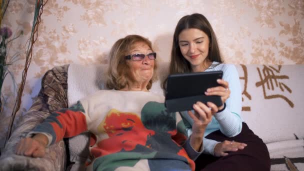 Volunteer girl teaches an elderly woman to use the screen tablet, home interior. — Stok Video