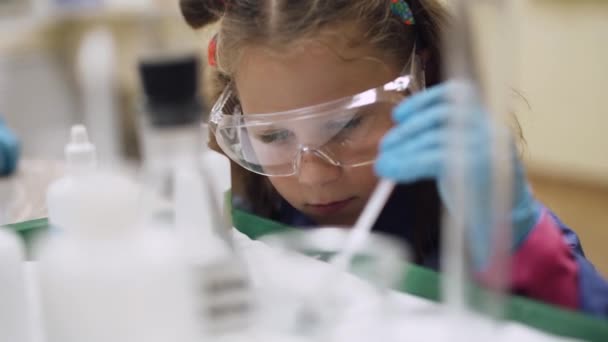 Laboratorio, un scoolgirl in occhiali di protezione mette esperienza chimica, educazione bambini. — Video Stock