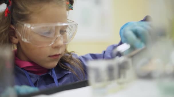 Laboratório, um scoolgirl em óculos protectores derrama líquido em tubo de ensaio, experiência de química, educação de filhos. — Vídeo de Stock