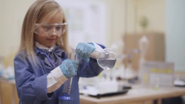 Laboratóriumi, egy védő szemüveg scoolgirl önti folyadék kémcsőbe, kémiai tapasztalat, gyermek oktatás. — Stock videók