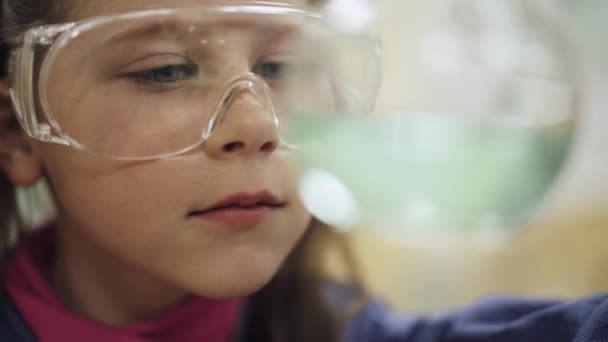 Лабораторія, школярка в захисних окулярах, вивчає рідину в скляній колбі, хімічний досвід, освіту дітей . — стокове відео