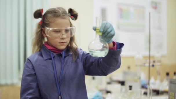 Лабораторія, школярка в захисних окулярах, вивчає рідину в скляній колбі, хімічний досвід, освіту дітей . — стокове відео