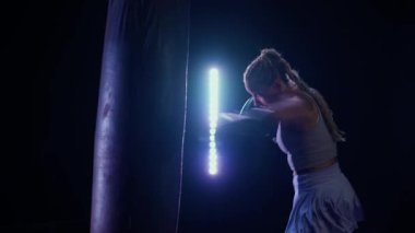 Ağır çekimde, kadın boksör kum torbasını yener, boks salonunda antrenman yapar, profesyonel dövüşçü tekmelerini ve yumruklarını eğitir, Kickboks yapar, vücudu sağlamdır..