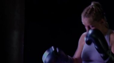 Hareket bulanıklığı, profesyonel kadın boksör yumruklarını eğitiyor, boks salonunda sıkı antrenman yapıyor, kum torbasını, motivasyonu yeniyor..