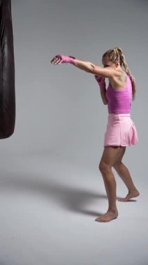 Kadın gücü, profesyonel boksör yumruklarını eğitiyor, beyaz boks salonunda antrenman yapıyor, kadın kickboksör pembe kumaş içinde bir dizi yumruk, yan görüş..