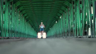 Varşova, Polonya - 20 Eylül 2025: Ağır çekim, sabah koşusu, nehrin üzerindeki köprüde koşan sportif kadın, tünelin alt açısı, yarı maraton antrenmanı.