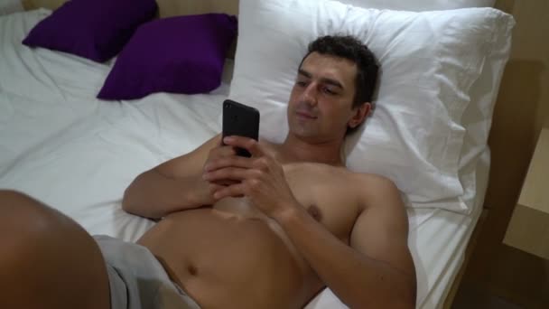 Homem relaxante na cama e lendo no smartphone, close, steadycam tiro, atividade de lazer — Vídeo de Stock