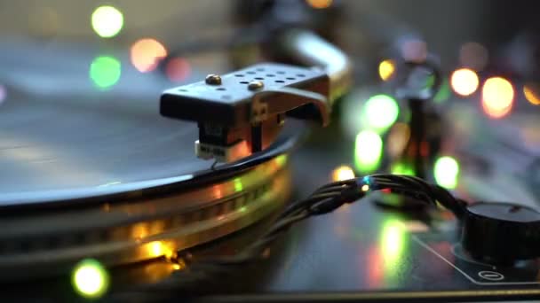 O disco de vinil no DJ toca-discos de perto. A placa rotativa e o estilete com a agulha de perto. Loop. brilhando bokeh luzes festivo humor feriados conceito — Vídeo de Stock