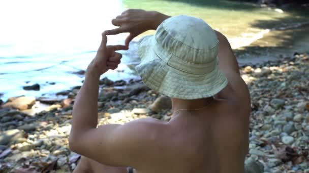Веселый Молодой Человек Сидящий Диком Красивом Пляже Делая Раму Руками — стоковое видео