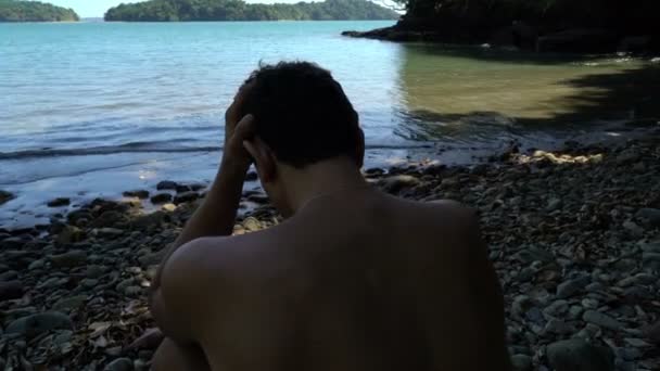 Onrustige jongeman zittend op het strand en het bedrijf van zijn hand, eenzaamheid, depressie, opressed — Stockvideo