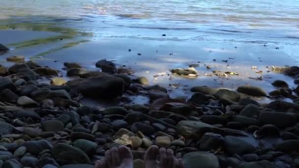 Jovens mulheres pernas em uma praia de pedras, ondas salpicando a costa em um dia ensolarado, pontos de vista — Vídeo de Stock