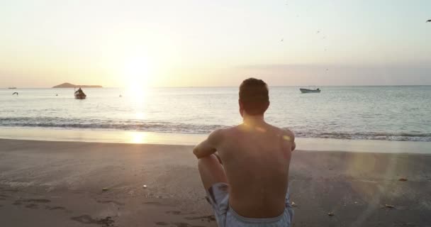 Young caucasian man relaxingon the beach near calm sea. Meeting sunrise. Meditation nature — Stock Video