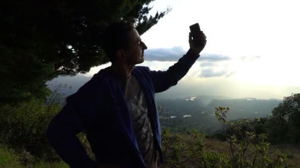 El hombre toma fotos de la puesta de sol dorada en las montañas con el teléfono de pie detrás de cerca en cámara lenta. Recuerdos fotográficos de vacaciones de verano con cámara móvil — Vídeos de Stock