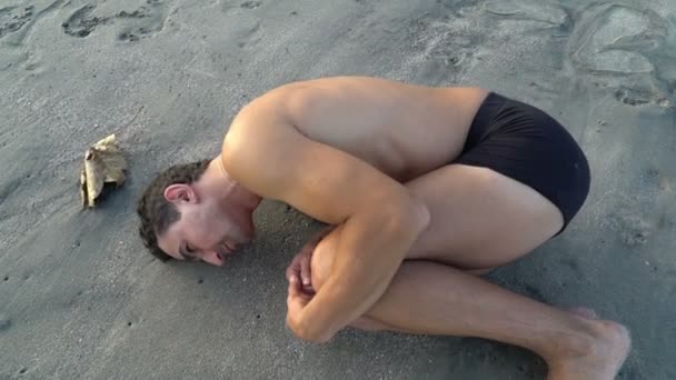 Man laying on the beach near the water in embryo pose. Evolution concept. Birth. Origin from the — Stock Video