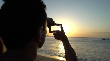 Fotoğraf çerçevesi tarafından elleri günbatımı üzerinde yapma adam