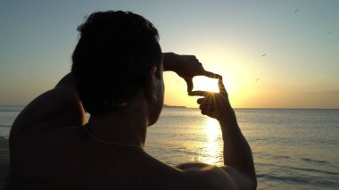 Fotoğraf çerçevesi tarafından elleri günbatımı üzerinde yapma adam