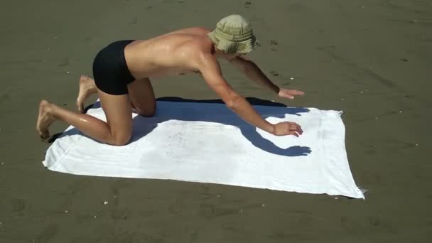 Uomo che cade su un asciugamano sulla spiaggia di sabbia da solo, non facendo nulla — Video Stock