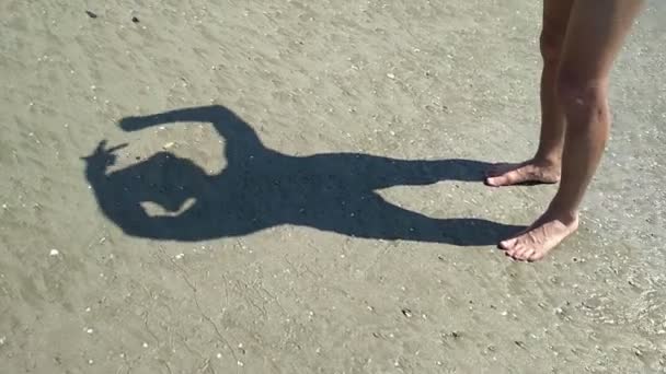 Homem na praia brincando com sua sombra na areia, ficando louco de ociosidade em ambiente incomum — Vídeo de Stock