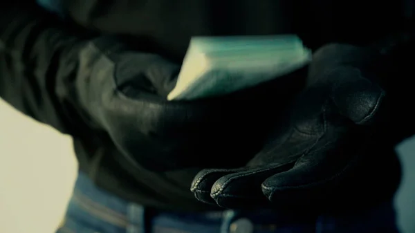 Человек в черных перчатках держит в руках кучу денег, преступную концепцию Стоковая Картинка