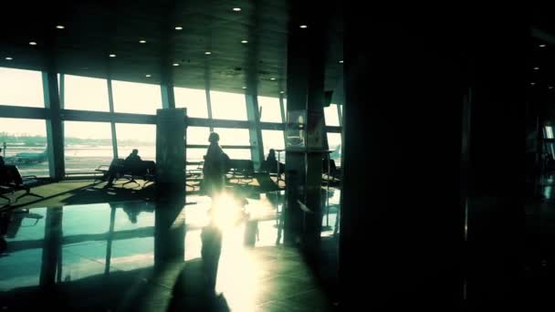 Silhouette de femme avec valise marchant à travers le hall à l'aéroport, au ralenti, soleil brillant — Video