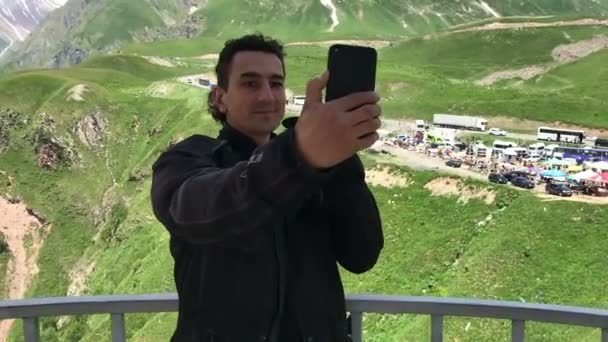 Ενήλικος χωρίς ξυρισμένη άνθρωπος. Παίρνει μια selfie στο smartphone του. Grimacing, προσωπογραφία, σε πράσινα βουνά — Αρχείο Βίντεο