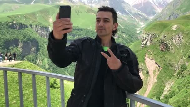 Hombre adulto sin afeitar. Se hace una selfie en su smartphone. Grimacía, autorretrato, en montañas verdes — Vídeos de Stock