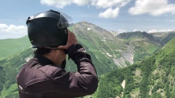 Man turist sätta av motorcykel hjälm och titta runt på punktvisa i grön kaukasiska — Stockvideo