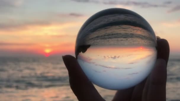 Mano femenina sosteniendo en las manos bola cristalina sobre hermosa puesta de sol de playa — Vídeo de stock