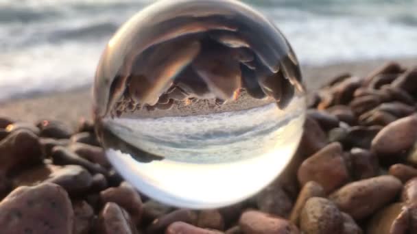 Paisagem de fundo beatiful dentro bola de cristal colocar em pedras de praia, pôr do sol e ondas do oceano dentro — Vídeo de Stock