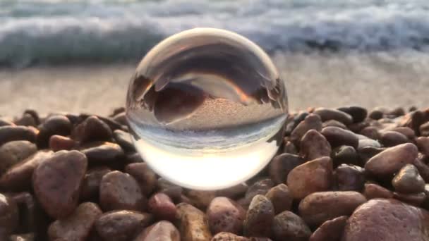 Paisagem de fundo beatiful dentro bola de cristal colocar em pedras de praia, pôr do sol e ondas do oceano dentro — Vídeo de Stock